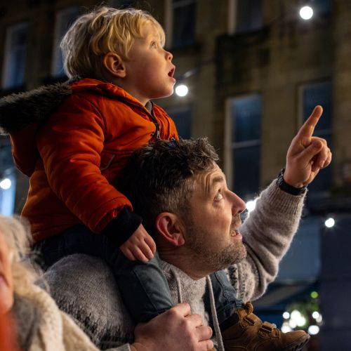 child sitting on adult's shoulders, looking up at something